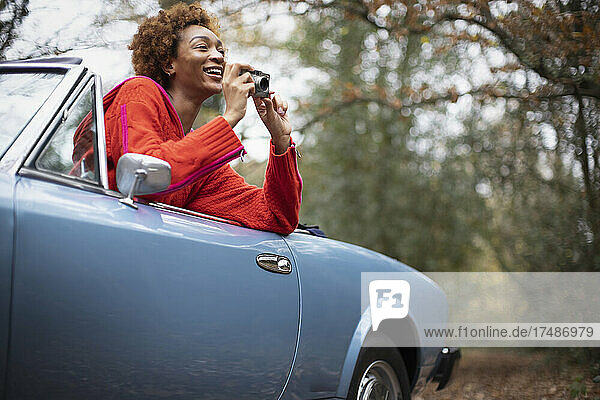 Happy young woman with digital camera in convertible in park
