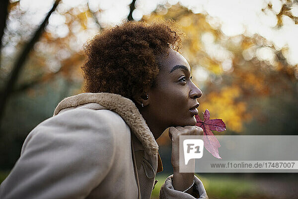Nachdenkliche junge Frau mit rotem Herbstblatt im Park