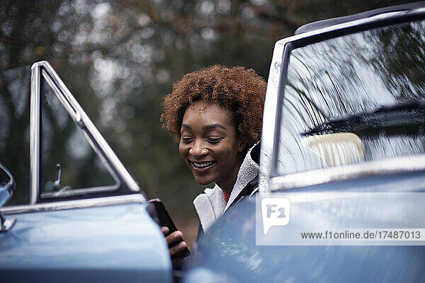 Glückliche junge Frau  die ein Smartphone im Cabrio benutzt
