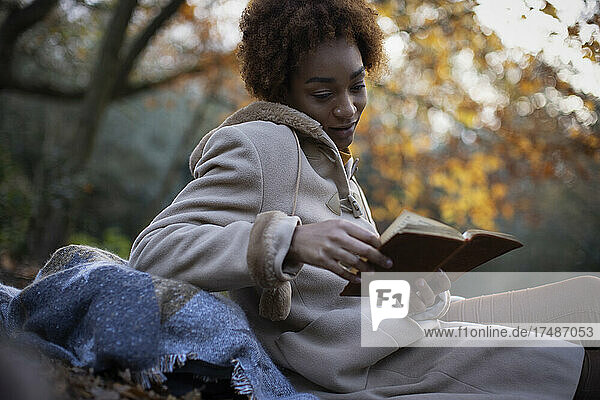 Junge Frau  die im Herbst in einem Park ein Buch liest