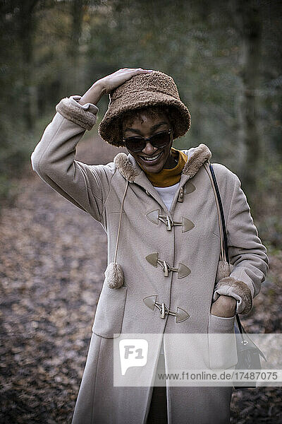 Glückliche junge Frau in Mantel und Hut im herbstlichen Park
