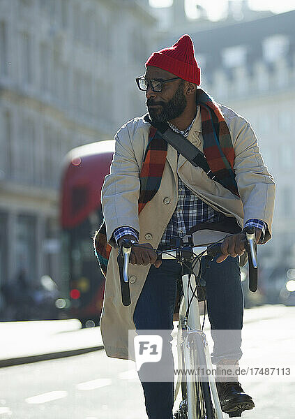 Businessman in stocking cap riding bike on sunny city street