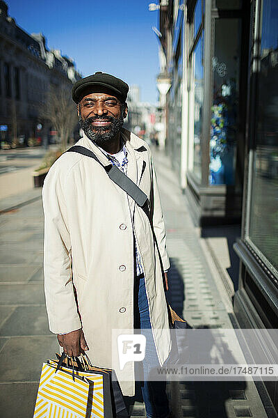 Porträt eines glücklichen Mannes mit Einkaufstüten vor einem sonnigen Geschäft in der Stadt