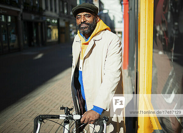 Porträt gut aussehender Mann mit Fahrrad vor einem sonnigen Schaufenster in der Stadt