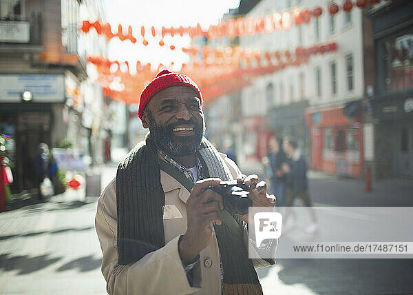 Portrait happy male tourist with digital camera on sunny city street