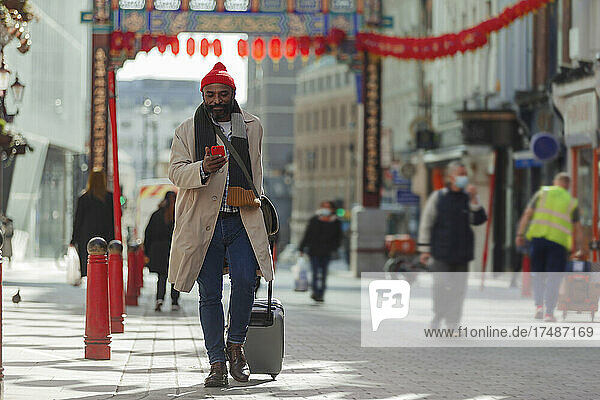 Male tourist with suitcase and smart phone at Chinatown Gate  London
