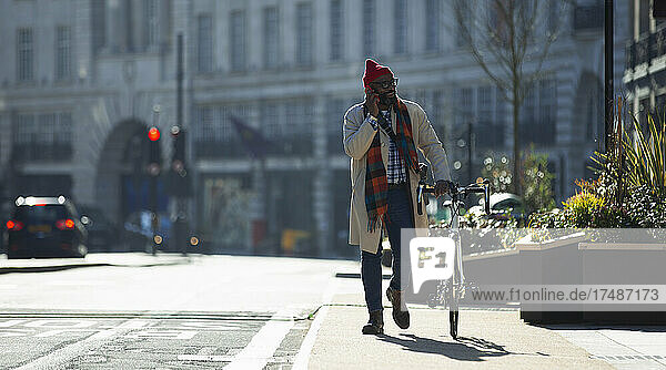 Geschäftsmann mit Fahrrad  der in einer sonnigen Stadt mit seinem Smartphone telefoniert