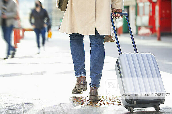 Male tourist pulling suitcase on city sidewalk