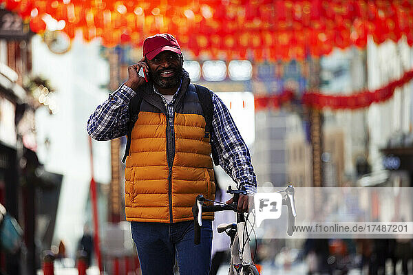 Man with bicycle talking on smart phone in city