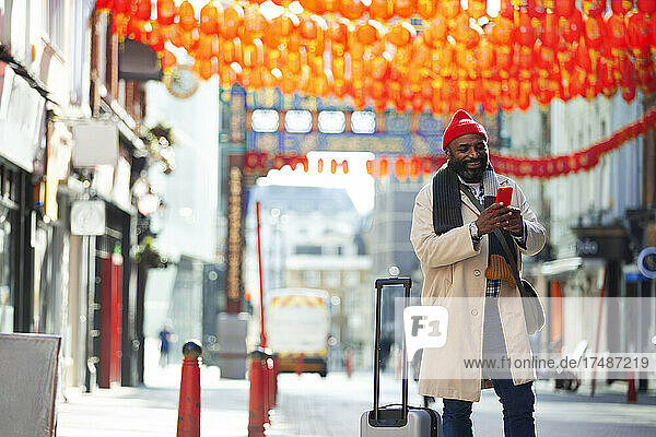 Männlicher Tourist mit Smartphone und Koffer auf einer Straße in London  Großbritannien