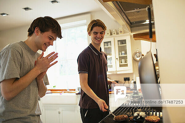 Glückliche Teenager-Jungs grillen Hamburger am Küchenherd