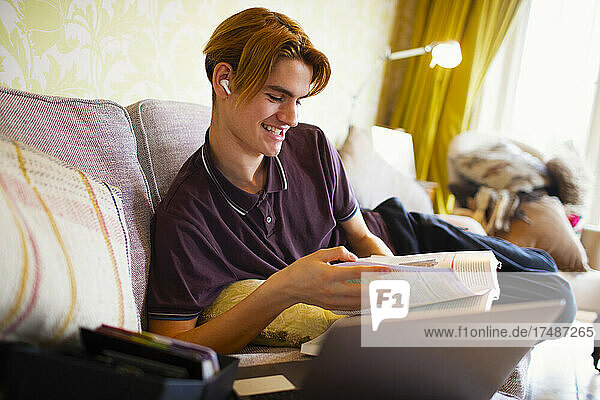 Smiling teenage boy with textbook and laptop studying at home
