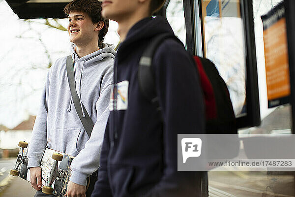 Lächelnder Jugendlicher mit Skateboard an der Bushaltestelle