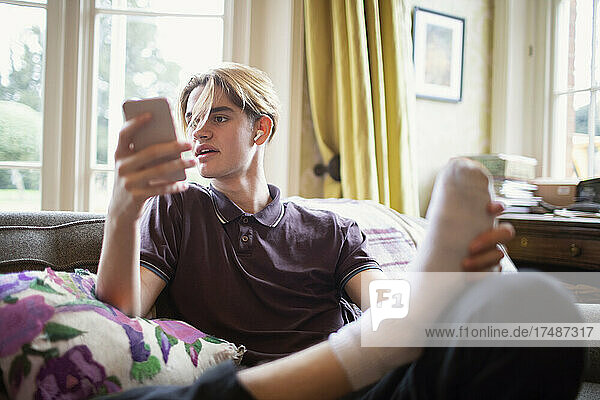 Teenage boy using smart phone at on living room sofa