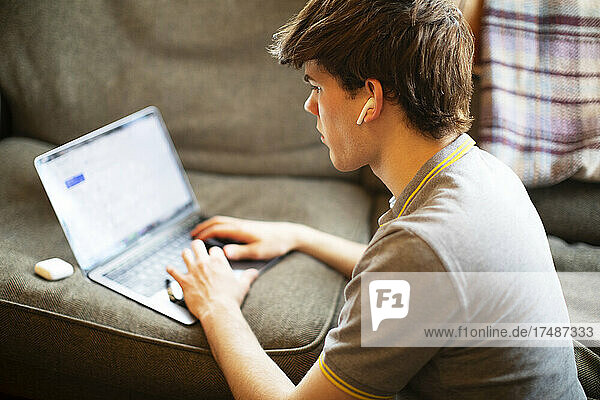 Jugendlicher mit Ohrstöpseln und Laptop auf dem Sofa zu Hause