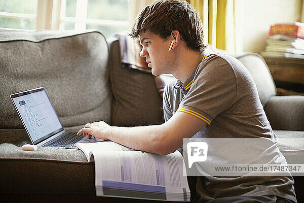 Focused teenage boy with laptop doing homework in living room