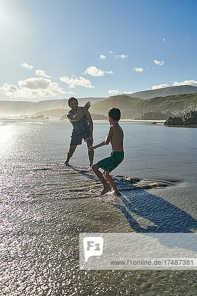 Playful father splashing son on sunny summer beach