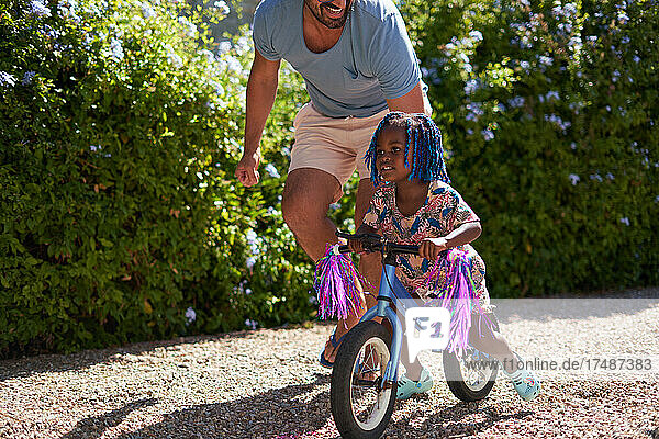 Vater hilft seiner kleinen Tochter beim Fahrradfahren in einer sonnigen Einfahrt