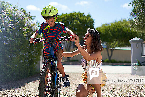 Mutter hilft ihrem Sohn in einer sonnigen Einfahrt  Fahrrad fahren zu lernen