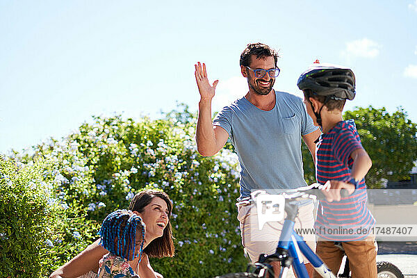 Glücklicher Vater und Sohn auf dem Fahrrad  die sich in der sonnigen Einfahrt die Hände reichen