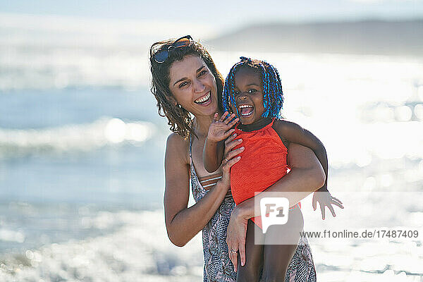 Portrait happy mother and cute toddler daughter on sunny ocean beach