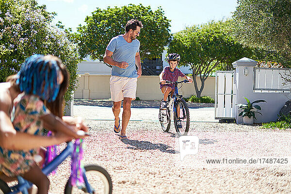 Father and son running and riding bike in sunny driveway