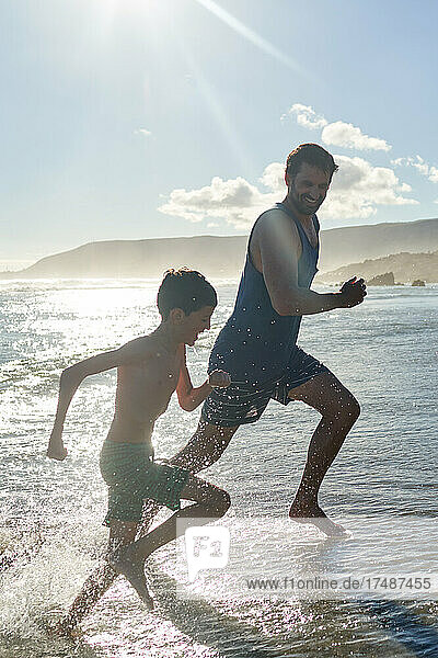 Glücklicher Vater und Sohn laufen in der sonnigen Sommerbrandung des Ozeans
