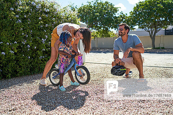 Parents and toddler daughter with bike in sunny summer driveway