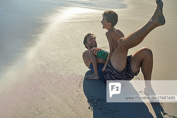 Glücklicher Vater und Sohn spielen am sonnigen Strand