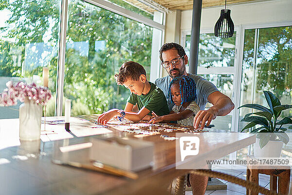 Vater und Kinder beim Zusammensetzen eines Puzzles am Esstisch