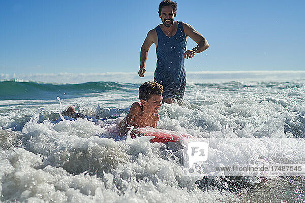 Happy father and son body boarding in sunny ocean surf
