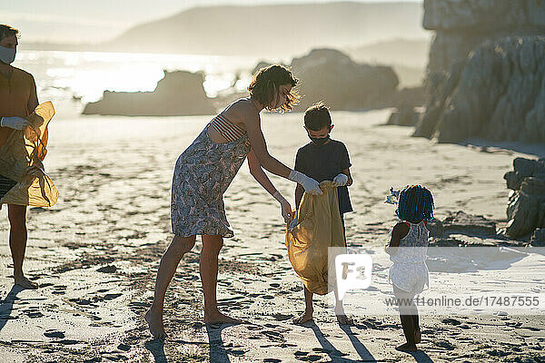 Familie mit Gesichtsmasken sammelt Müll am sonnigen Strand auf