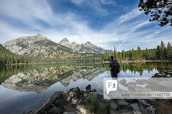 Young man standing by a lake  reflection in Taggart Lake  view of Teton Range mountain  peaks Grand Teton and Teewinot Mountain  Grand Teton National Park  Wyoming  USA  North America