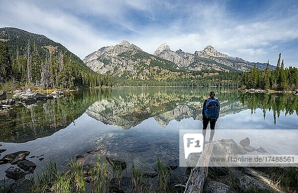 Young woman standing at a lake  reflection in Taggart Lake  view of Teton Range mountain  peaks Grand Teton and Teewinot Mountain  Grand Teton National Park  Wyoming  USA  North America