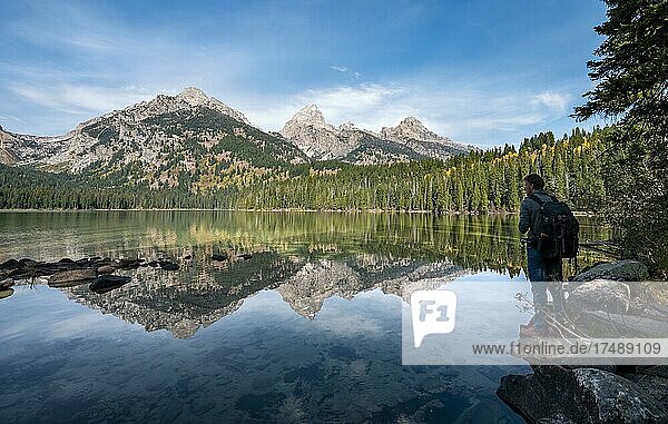Young man standing by a lake  reflection in Taggart Lake  view of Teton Range mountain  peaks Grand Teton and Teewinot Mountain  Grand Teton National Park  Wyoming  USA  North America