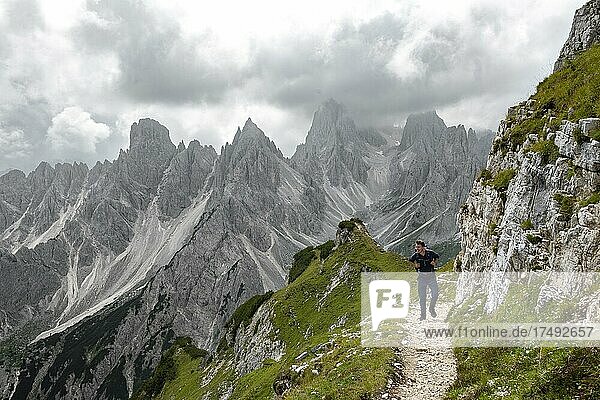 Hikers on a trail  mountain peaks and pointed rocks in the background  dramatic cloudy sky  Cimon di Croda Liscia and Cadini group  Auronzo di Cadore  Belluno  Italy  Europe