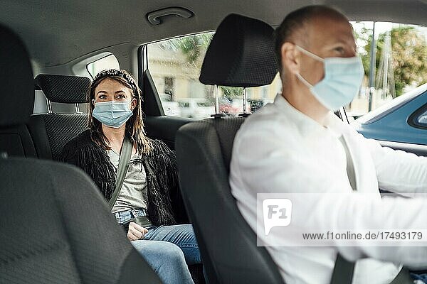 Taxifahrer in einer Maske mit einer weiblichen Kundin auf dem Rücksitz mit Maske