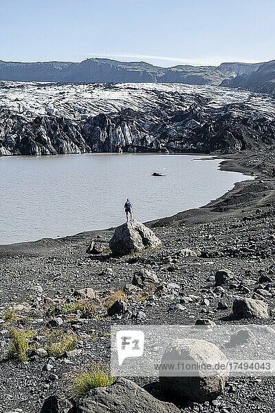 Wanderer steht auf Felsen vor Gletscherzunge Sólheimajökull am Gletscher Mýrdalsjökull  Suðurland  Island  Europa