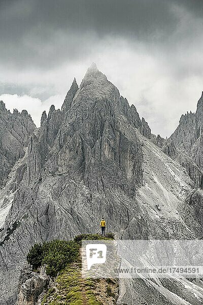 Hiker standing on a ridge  mountain peaks and pointed rocks behind  dramatic cloudy sky  Cimon di Croda Liscia and Cadini group  Auronzo di Cadore  Belluno  Italy  Europe