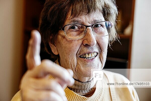 Seniorin mit erhobenen Zeigefinger zuhause in ihrem Wohnzimmer  Köln  Nordrhein-Westfalen  Deutschland  Europa