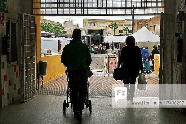 Mann mit Kinderwagen und Frau mit Einkaufstüten verlassen Markthalle  im Gegenlicht