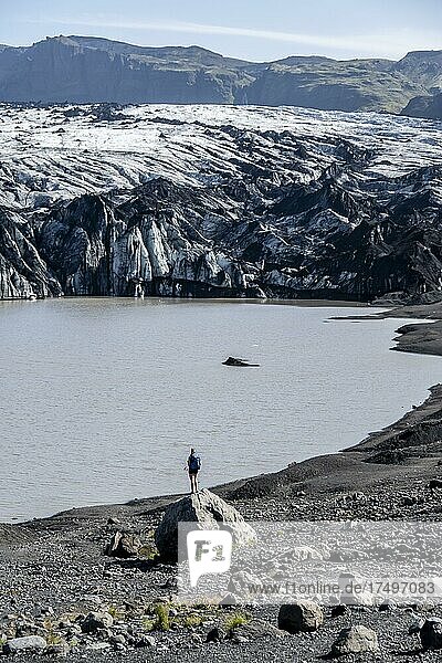 Hiker standing on rocks in front of glacier tongue Sólheimajökull at glacier Mýrdalsjökull  Suðurland  Iceland  Europe