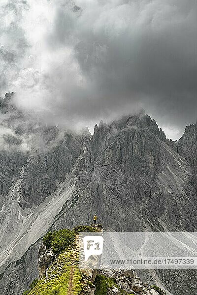 Hiker standing on a ridge  mountain peaks and pointed rocks behind  dramatic cloudy sky  Cimon di Croda Liscia and Cadini group  Auronzo di Cadore  Belluno  Italy  Europe