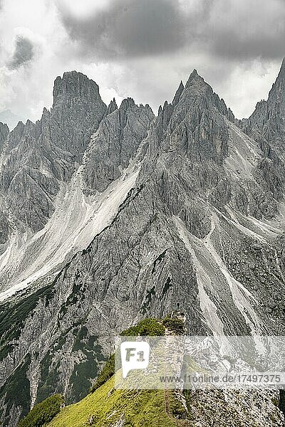 Wanderin steht auf einem Grat  hinten Berggipfel und spitze Felsen  dramatischer Wolkenhimmel  Cimon di Croda Liscia und Cadini-Gruppe  Auronzo di Cadore  Belluno  Italien  Europa