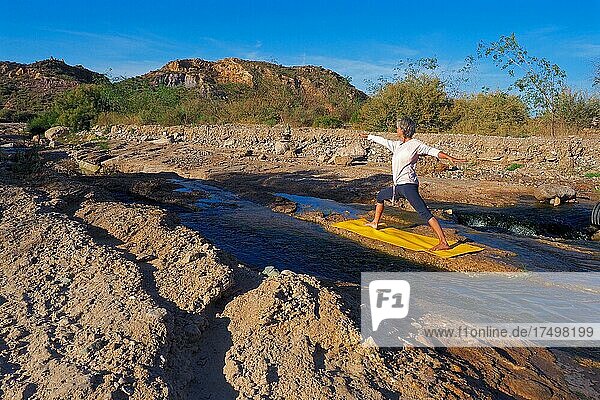 Woman doing yoga on mat by the river  yoga outdoors  yoga exercise in nature  Andalucia  Spain  Europe