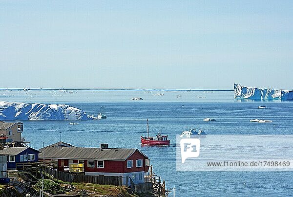 Wohnhäuser und Fischerboot am Rande einer mit Eisbergen bedeckten Bucht  Ilulissat  Arktis  Diskobucht  Grönland  Arktis  Dänemark  Nordamerika
