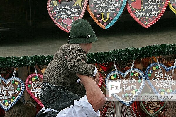 Mann vor Stand mit Zuckerherzen trägt Kind mit Filzhut auf den Schultern  Oktoberfest  München  Bayern  Deutschland  Europa