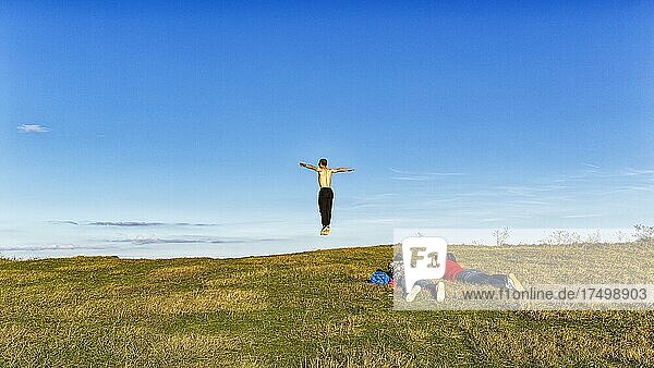 Junge Leute am Rand einer Klippe  Mann springt in die Luft  Arme ausgebreitet  Beachy Head  Eastbourne  East Sussex  England  Großbritannien  Europa