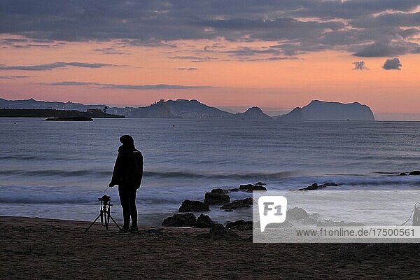 Photographer with camera and tripod in the morning at the sea  morning atmosphere at the sea with photographing woman  sunrise at the beach with view to Aguilas and Cabo Cope  Murcia  Spain  Europe