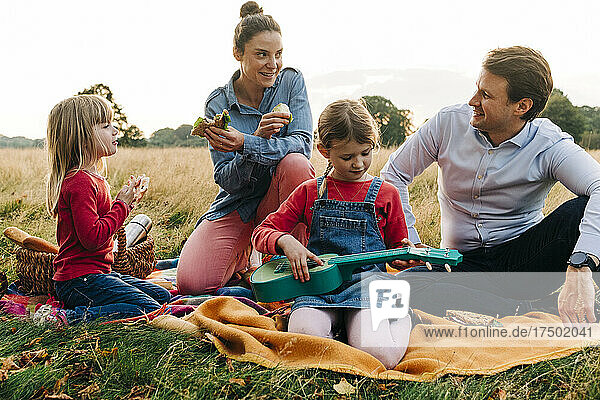 Smiling parents sitting with daughters on picnic blanket